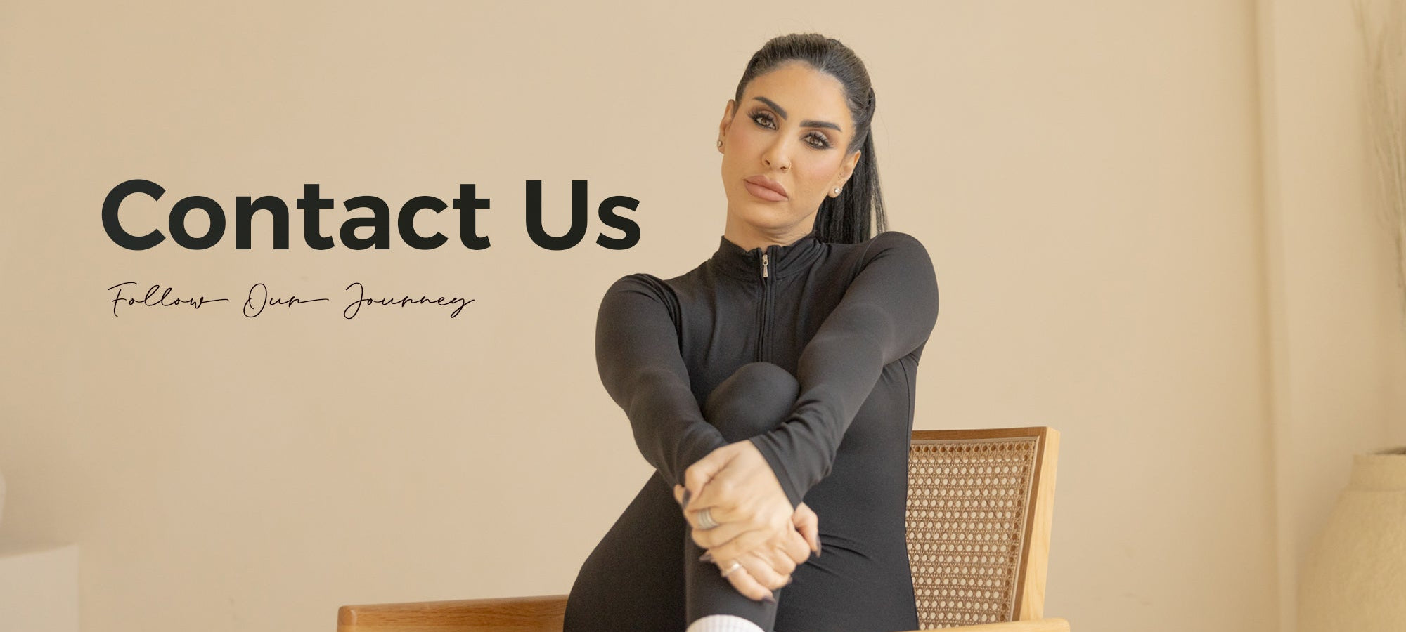 Woman in a black outfit sitting on a chair with 'Contact Us' text on a beige background
